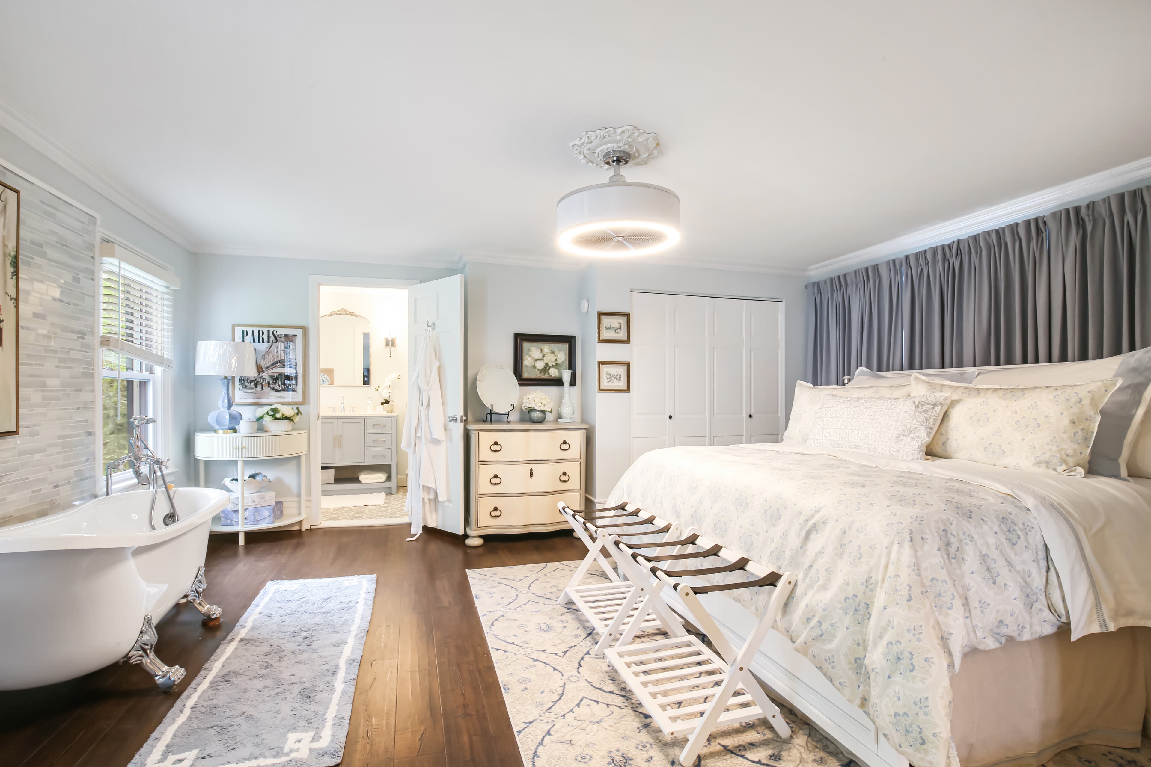 A beautifully styled bedroom featuring a large bed, vintage furniture, and an elegant freestanding bathtub.
