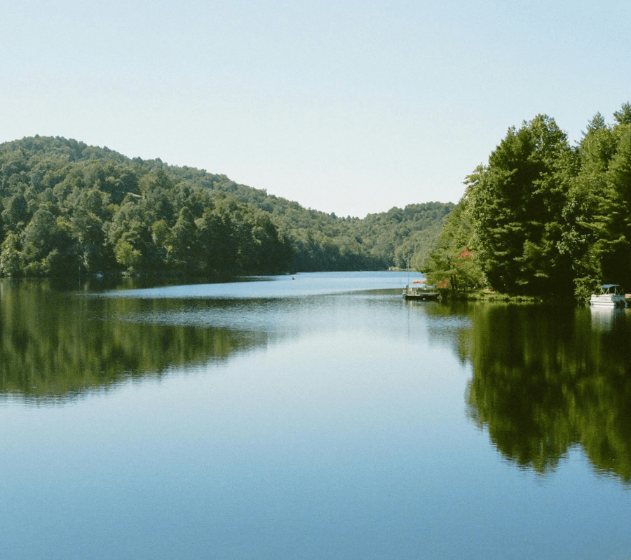 A tranquil lake reflecting surrounding hills and trees under a clear blue sky.