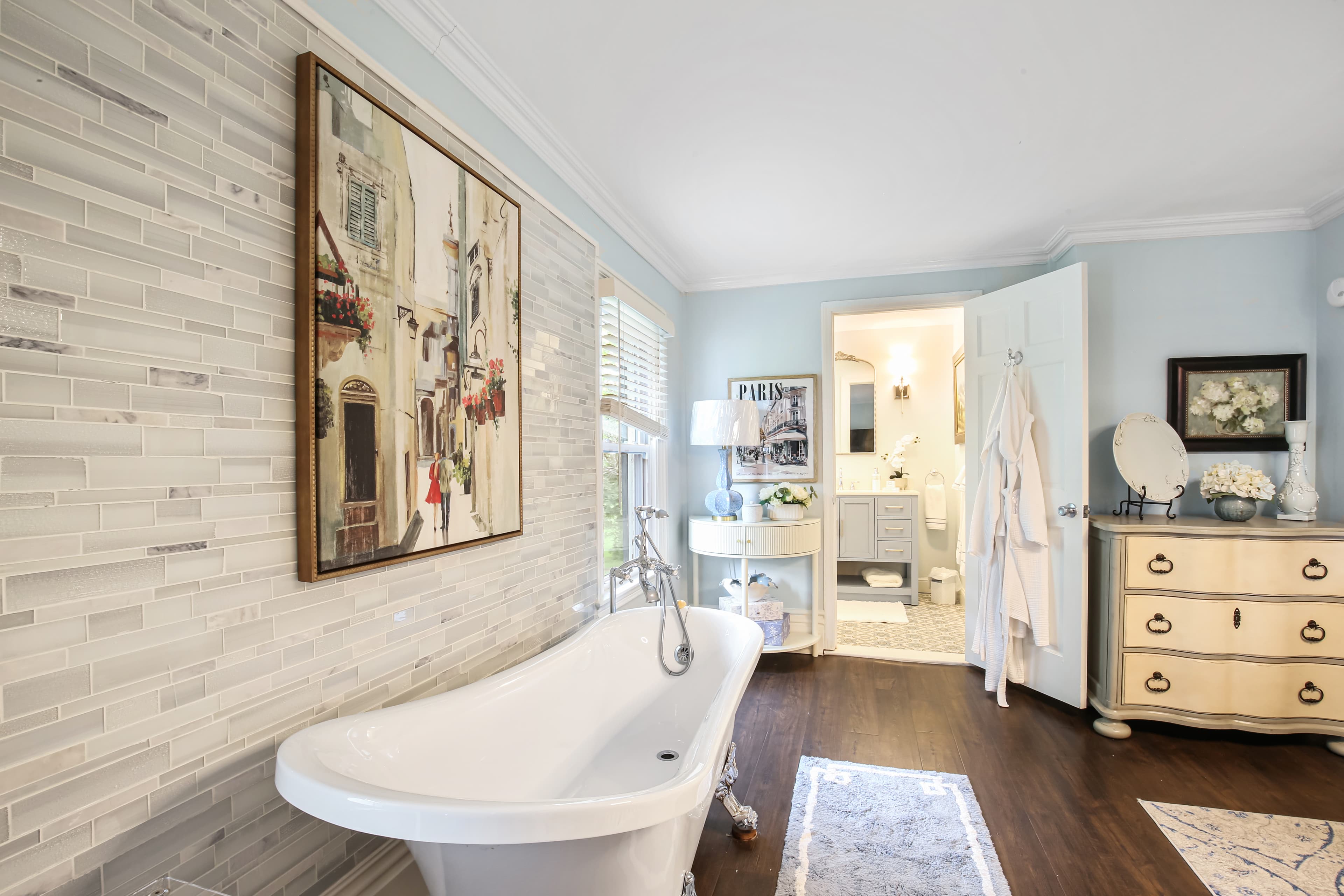 A bright, modern bathroom featuring a freestanding bathtub, decorative wall art, and stylish furnishings.