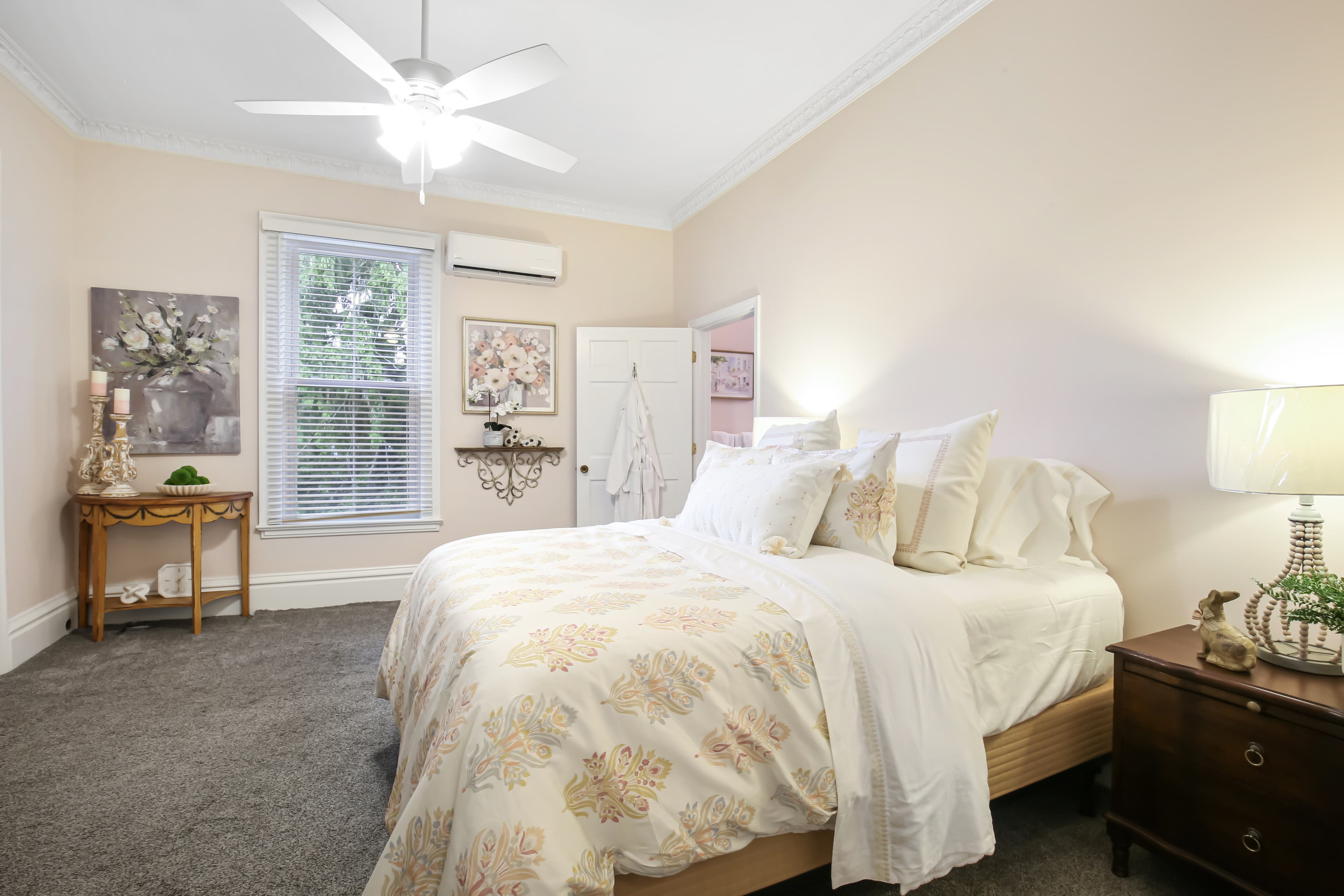 A cozy bedroom featuring a bed with a floral quilt, nightstand, and decorative artwork on the walls.