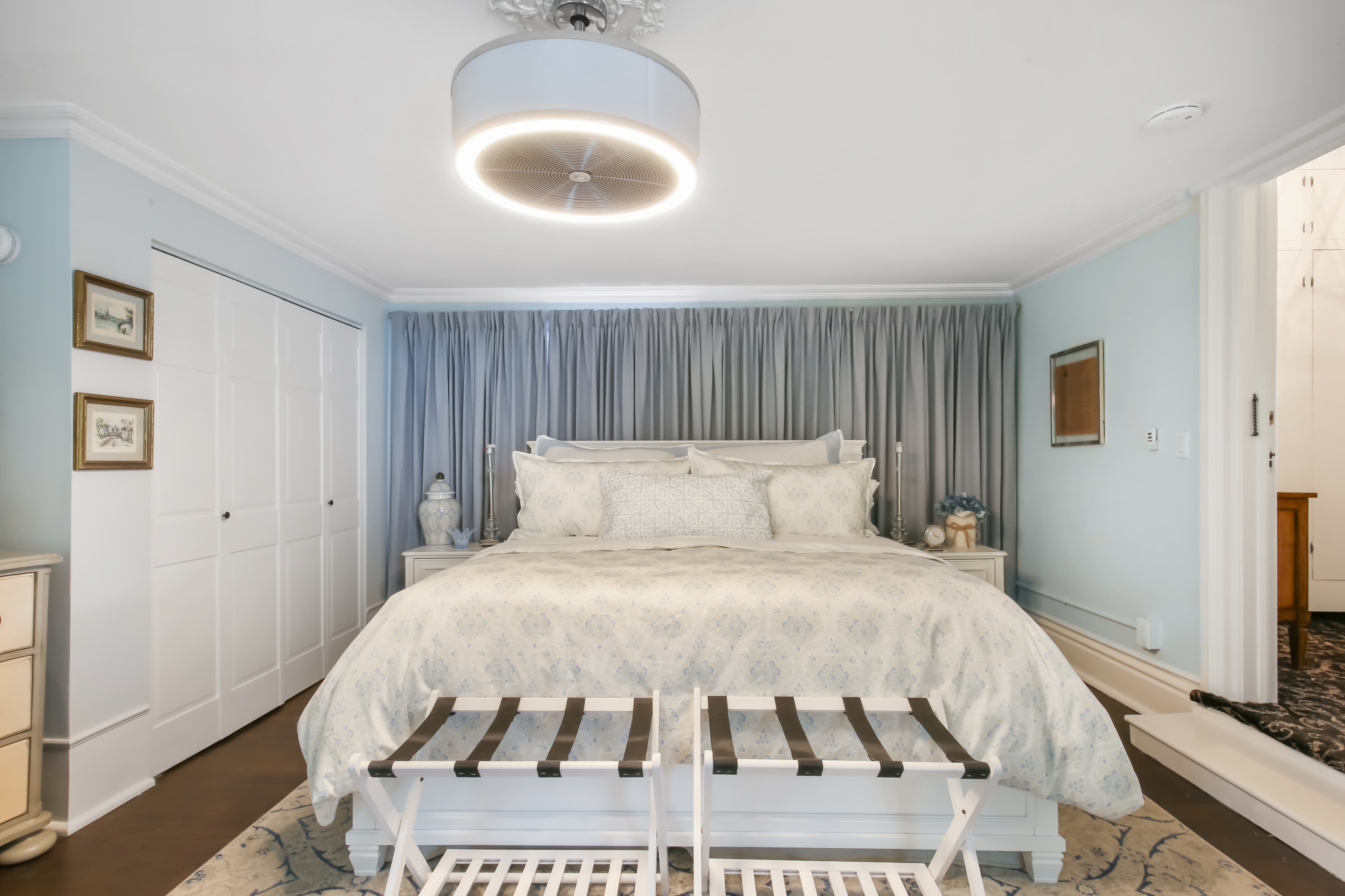 A modern bedroom featuring a large bed, decorative pillows, and a stylish light fixture, with soft blue walls and sliding closet doors.