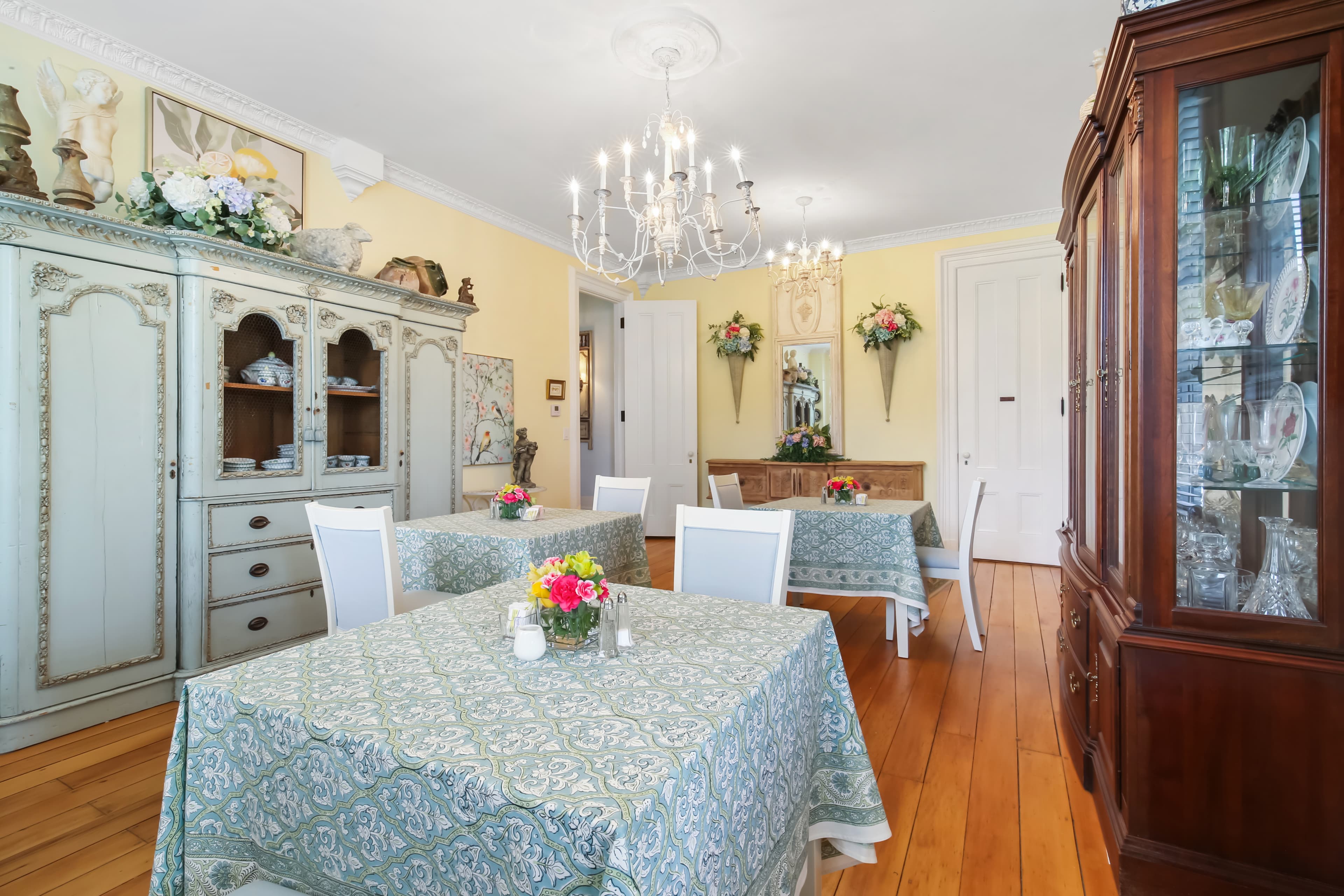 A charming dining room featuring floral tablecloths, elegant chandeliers, and vintage furnishings.