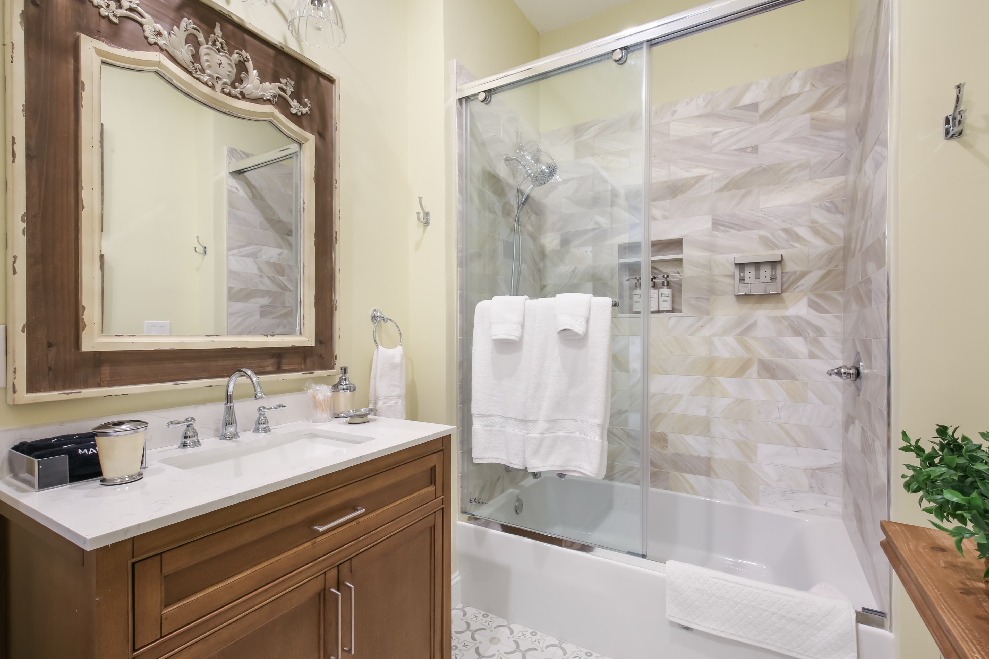 A modern bathroom featuring a glass shower, decorative mirror, and wooden vanity with sink.