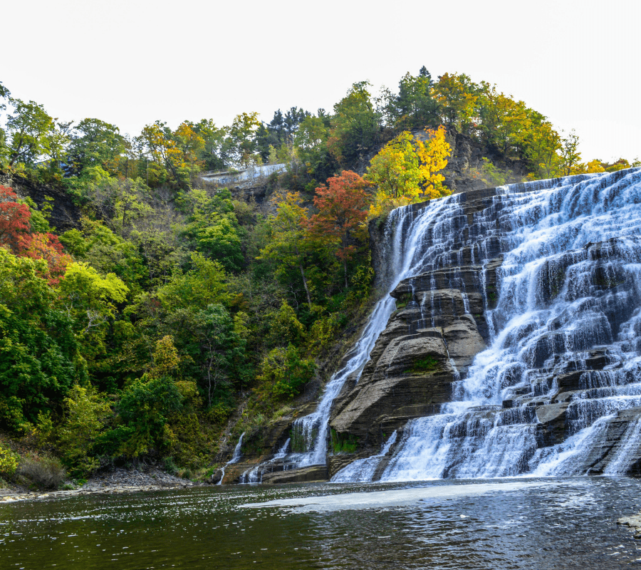 A cascading waterfall flows down a rocky cliff surrounded by vibrant autumn foliage.